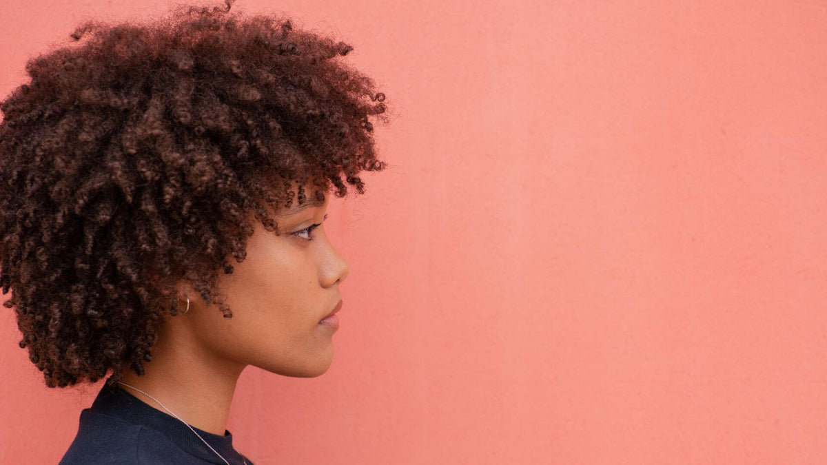 woman with short coily hair on pink background