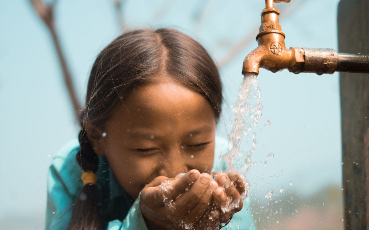 A girl drinks clean water from a tap at a charity: water project