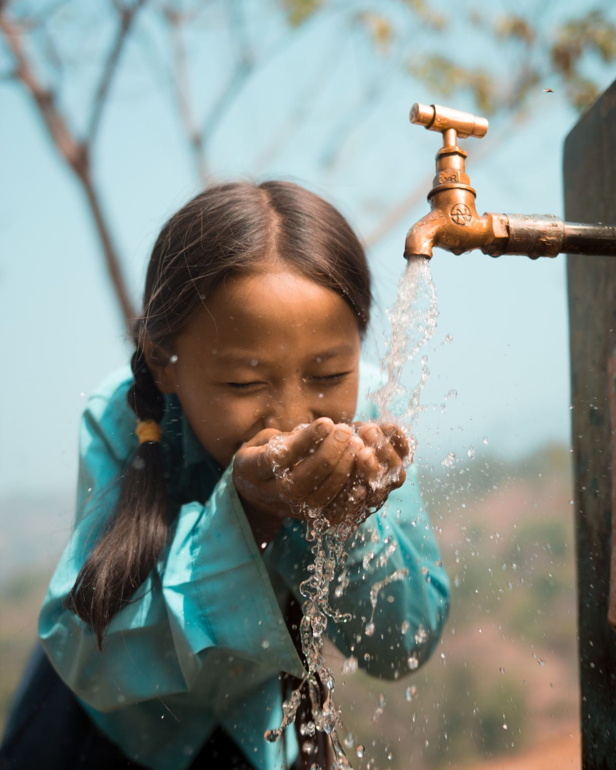 A girl drinks clean water from a tap at a charity: water project